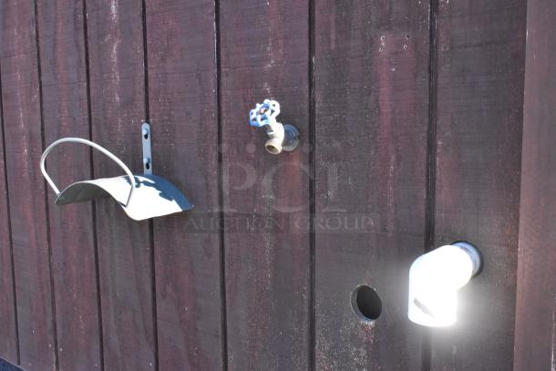 Exterior view of a food trailer with a water spigot, light fixture, and metal bracket on dark wooden siding.
