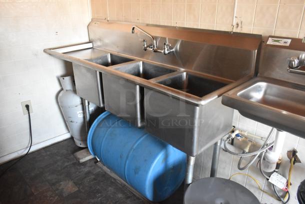 Stainless steel triple sink setup in a food trailer with propane tank and blue barrel below. Clean condition.