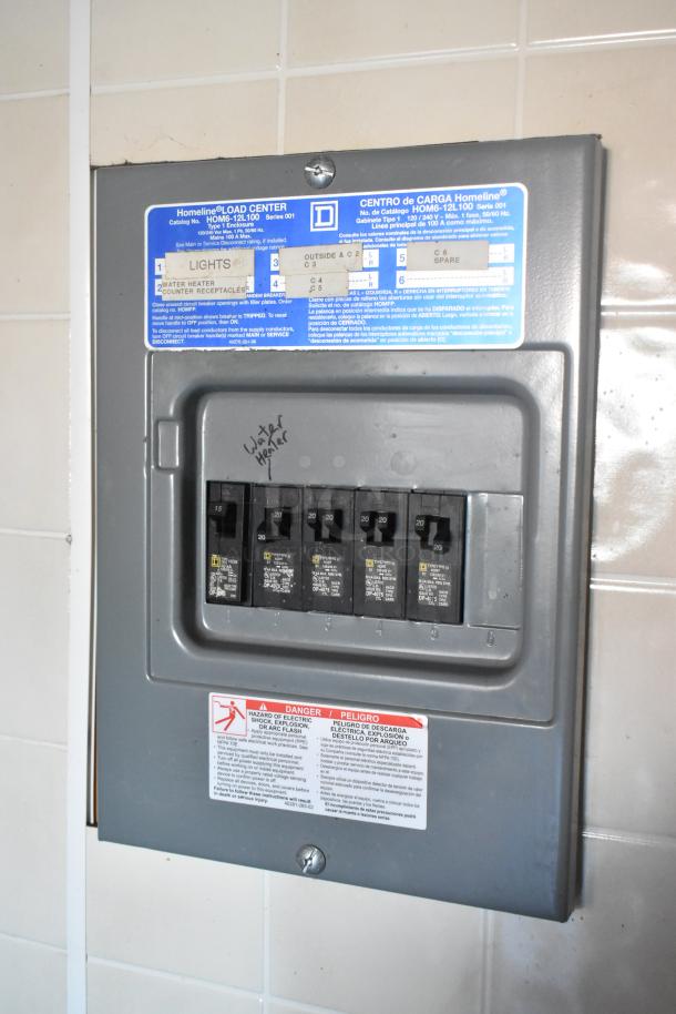 Electrical panel in a food trailer, labeled for lights and appliances, includes safety warnings. Homeline Load Center brand.