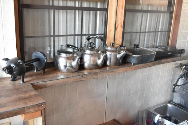 Food trailer interior with kettles, a pig-shaped utensil holder, and a Cuisinart griddle on a wooden shelf.