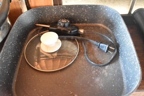 Electric skillet with a glass lid and power cord inside a food trailer. Includes adjustable temperature control knob.