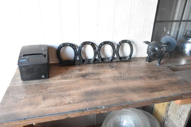 Wooden counter inside food trailer with horseshoe decor and small black pig statue. Features a black receipt printer labeled "SNBC."