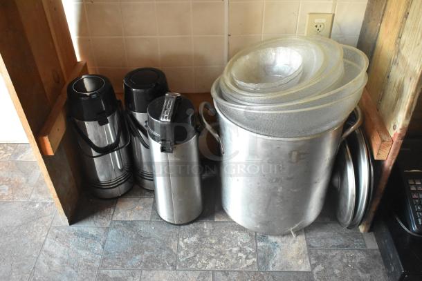 Stainless steel thermoses and a large pot with nested lids on a tiled floor in a mobile kitchen setup.