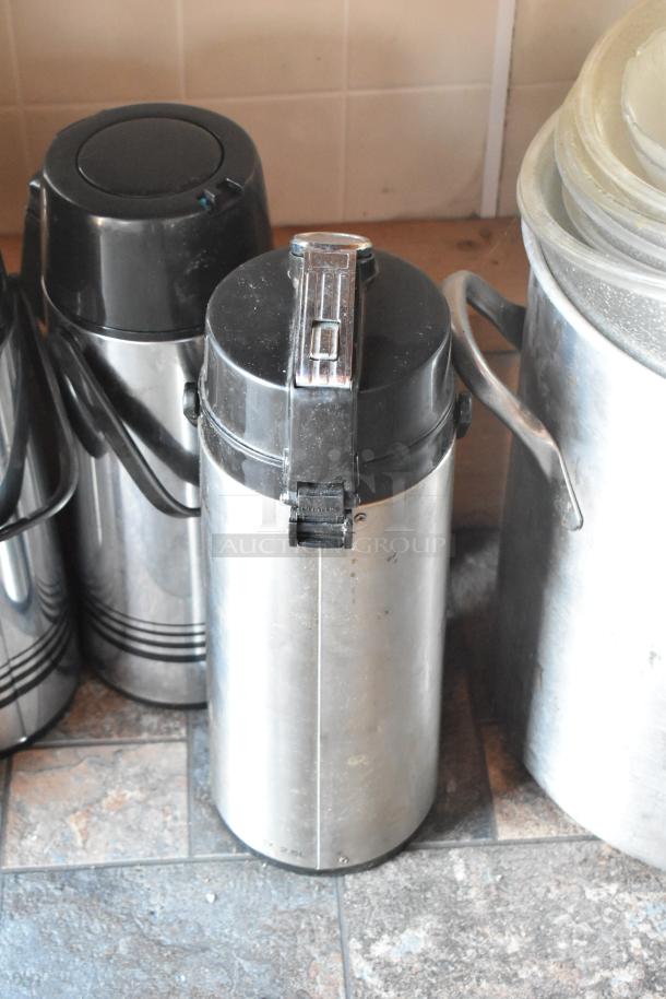 Stainless steel airpot thermal dispensers on a tiled surface, featuring secure lids and handles for easy pouring.