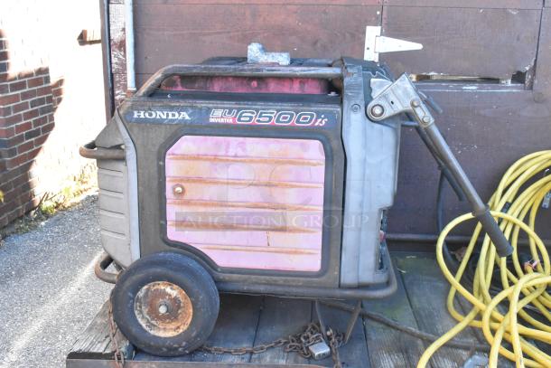 Honda EU6500is inverter generator, visible wear, attached to wheels, with yellow extension cords and chains nearby.