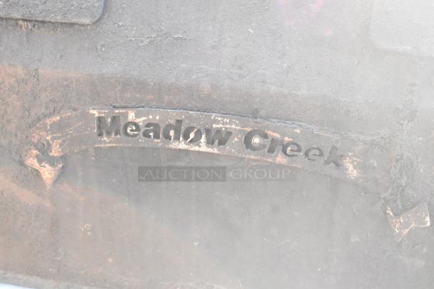 "Meadow Creek" branding on a barbecue grill, showing wear consistent with usage.