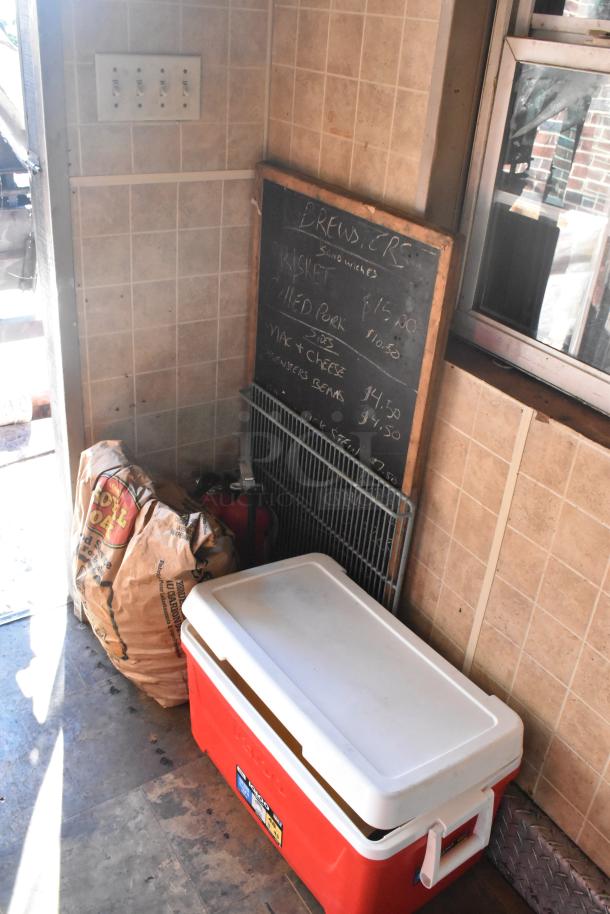 Interior of 2007 Lanchester food trailer with wooden menu board, large cooler, bag of charcoal, and wall switches.