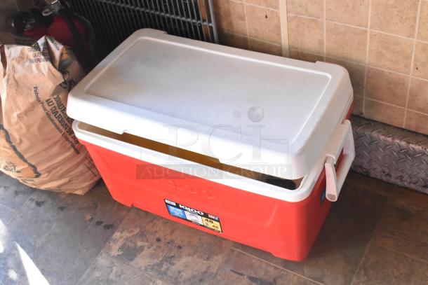 Red Igloo cooler on trailer floor, white lid, and side handles. Label shows 48 qt capacity.