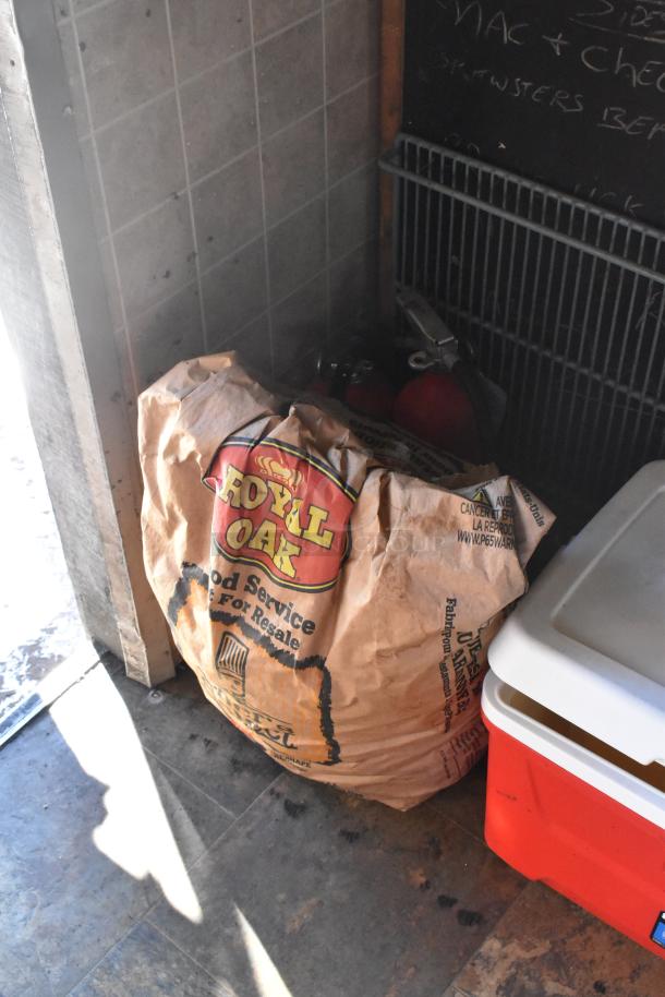 Bag of Royal Oak charcoal alongside a red cooler and chalkboard in a food trailer.