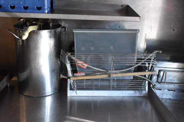 Commercial-grade stainless steel pot with large handles, wire rack, and flexible piping inside a stainless steel food trailer kitchen.