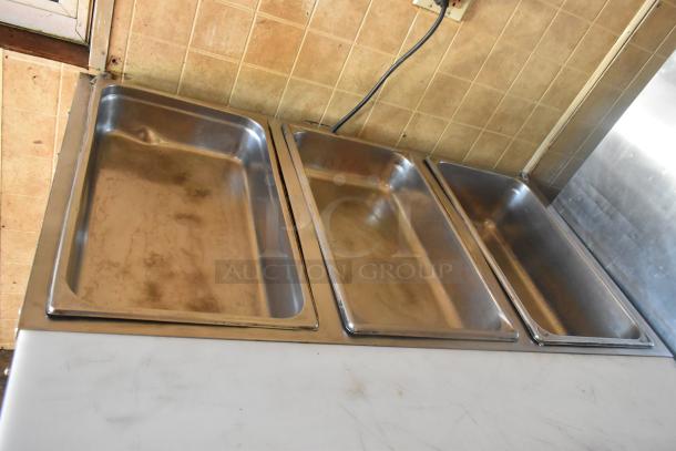 Three stainless steel steam table pans inside a 2007 Lanchester food trailer, set against a tiled wall.