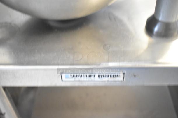 Stainless steel commercial mixer stand with attachment rod, metal under shelf, and casters. Service label visible.