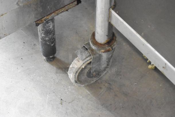 Stainless steel mixer stand with attachment rod, metal shelf, commercial casters; signs of use and surface rust.