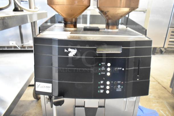 Schaerer Verismo 701 commercial espresso machine with dual hoppers, metal construction, visible control panel. Model tag reads "Verismo 701."