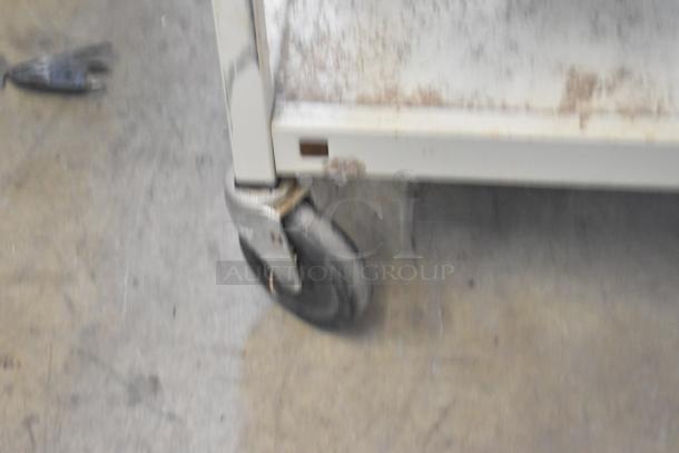 Metal 4-tier cart with commercial casters, showing some wear. Sturdy construction, ideal for heavy-duty storage.