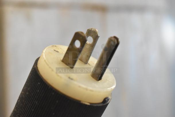 Three-prong electrical plug with a black textured grip handle, shown close-up.