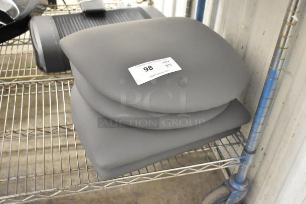 Four new gray seat cushions, slight cosmetic imperfections, stacked on a wire shelf. Auction label reads “98.”