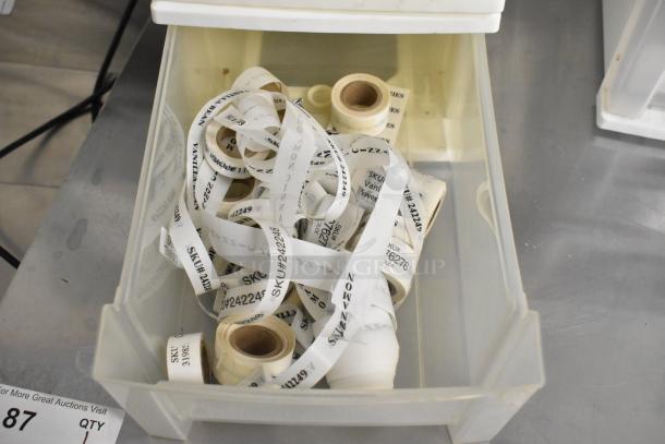 Four clear and white poly bins filled with assorted labeled tape rolls featuring SKU numbers. Signs of light use.
