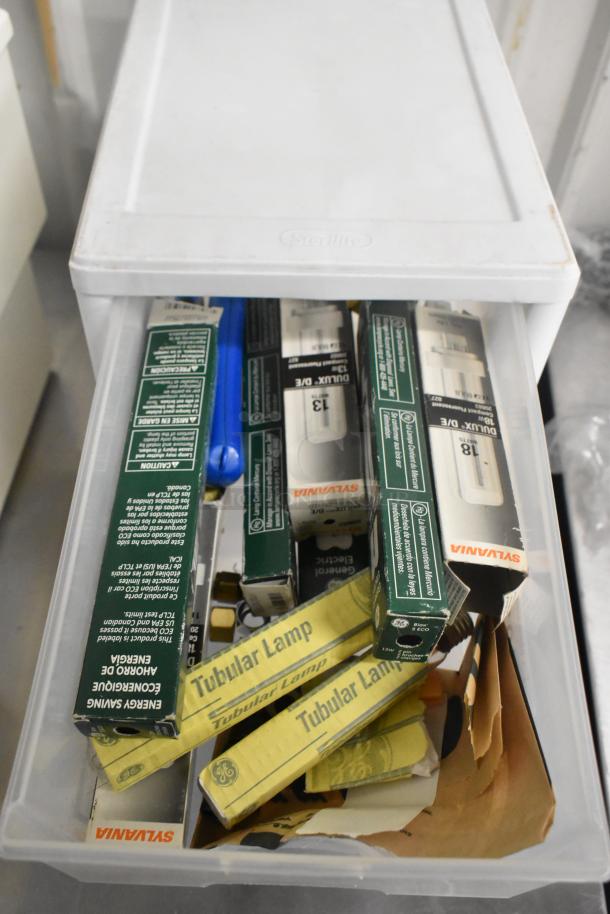 Clear poly bin with assorted contents including Sylvania and GE lamp boxes, indicating new tubular lamps and components.