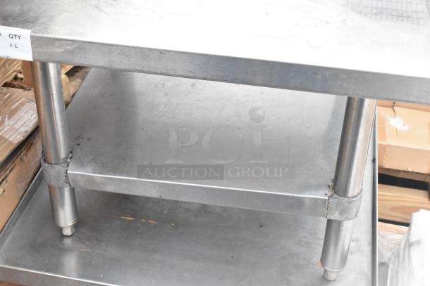 Stainless steel commercial equipment stand with under shelf, lightly used. Durable with visible surface wear. Tags indicate quantity x2.