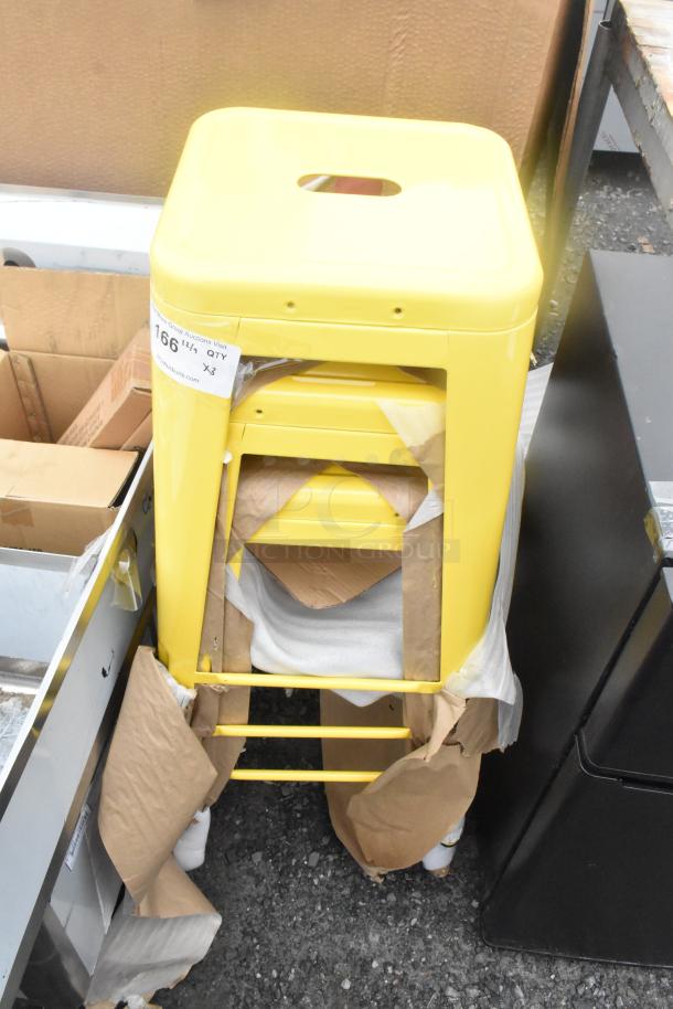 Three yellow metal Tolix-style stools, stacked, new condition, with protective packaging and auction label indicating quantity three.