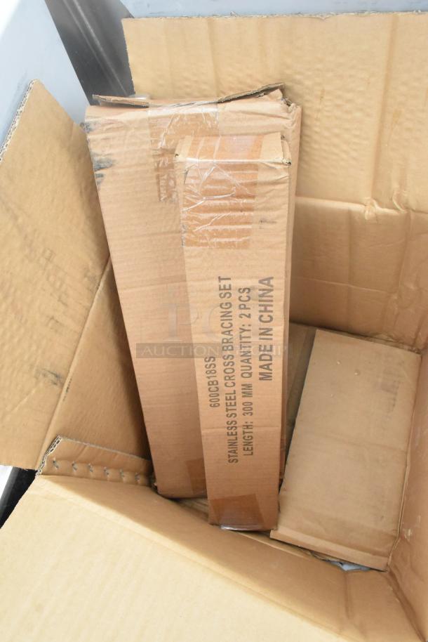 Alt text: Regency 600S3181818C stainless steel L-shaped 3-bay sink with dual drain boards in packaging. Visible markings include "600CB18SS Stainless Steel Cross Bracing Set Made in China." New with scratches and dents.