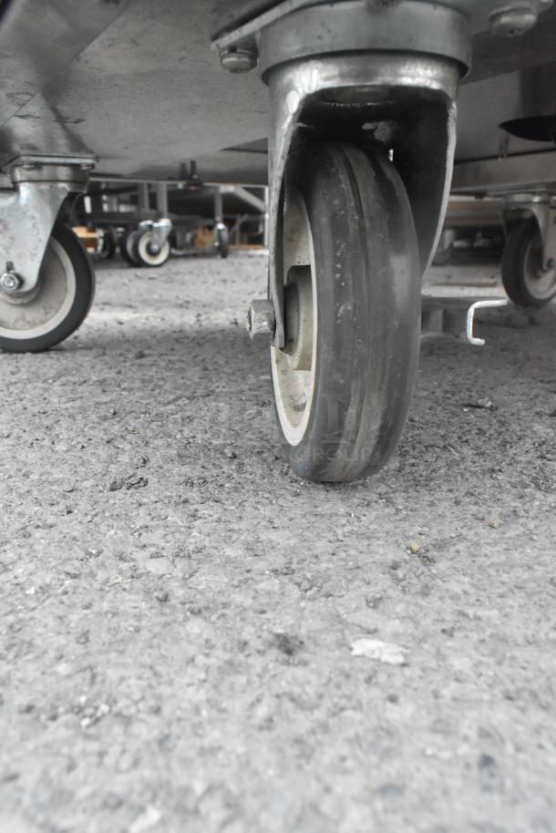 QualServ stainless steel portable sink caster, showing sturdy condition on a textured surface.