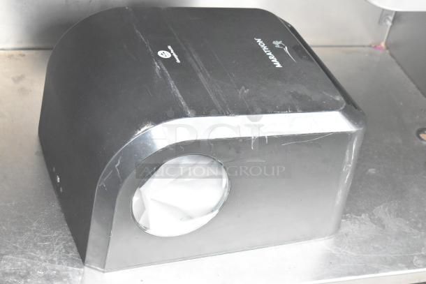 A black tabletop paper towel dispenser marked "Marathon" on a stainless steel table.