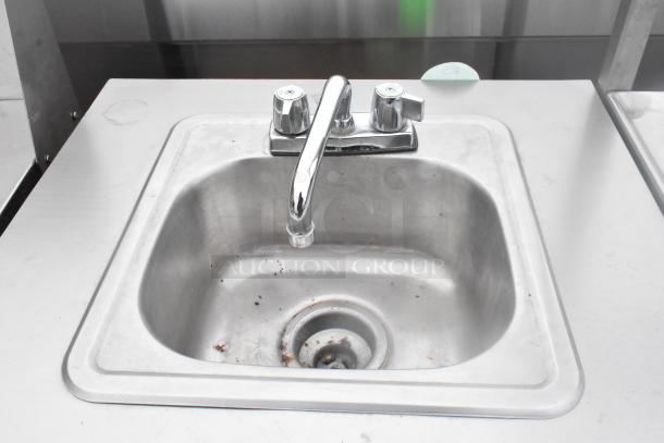 Metal single bay portable sink on commercial casters, stainless steel, dual handle faucet, visible wear, ideal for mobility.