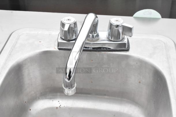 Metal single bay portable sink on commercial casters, chrome faucet, double handles labeled "hot" and "cold," slight surface wear.
