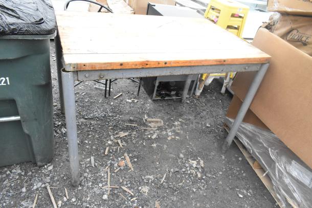Butcher block wooden table with metal legs, showing wear and exposed screws. Rustic condition, ideal for rustic or industrial decor.