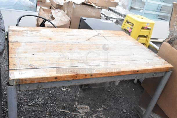 Butcher block wooden table with metal legs, well-worn surface, visible nicks, sticker showing "175 lbs" capacity.