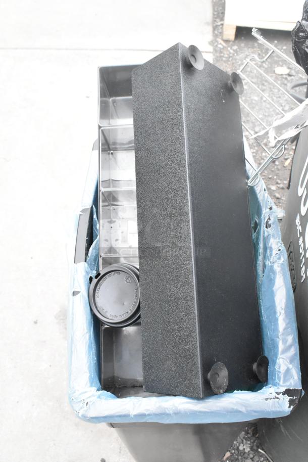 Two poly trash cans with mixed contents, including storage trays and lids. Sturdy condition, suitable for industrial use.