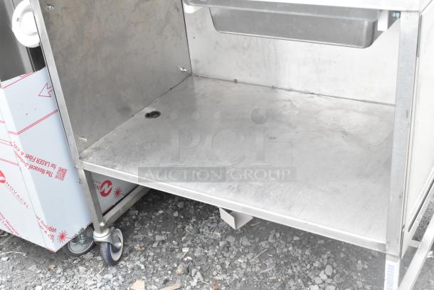 Stainless steel table with under shelf, commercial casters, and visible wear on surface. Ideal for industrial use.