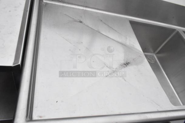 Stainless steel 3 bay sink with dual drain boards and under shelf. Slight wear visible, robust for commercial use.