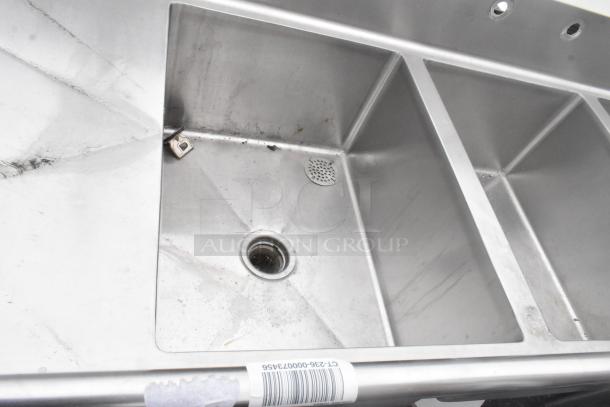 Stainless steel 3 bay sink with dual drain boards, under shelf, and visible barcode. Slight wear. Perfect for commercial use.
