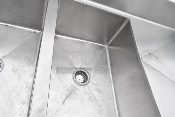Stainless steel 3 bay sink with dual drain boards and under shelf, showing light wear and visible drain fittings.