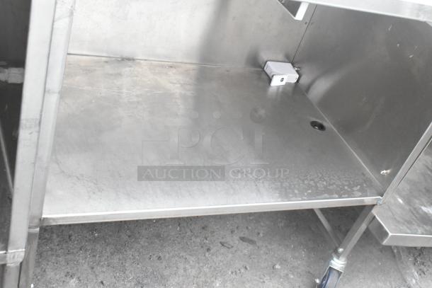 Stainless steel table with under shelf and commercial casters, showing minor surface wear, suitable for industrial use.