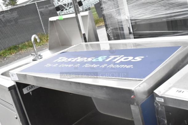 Stainless steel table with under shelf, drawer, and commercial casters. Includes sink and faucet, signage reads "Tastes & Tips."