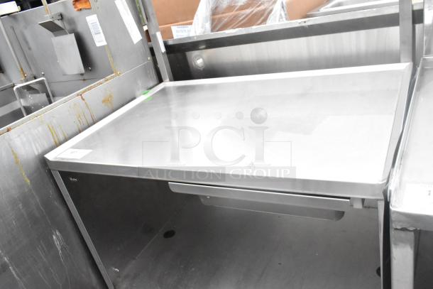 Stainless steel table with drawer, under shelf, and commercial casters; shows slight wear, suitable for industrial use.