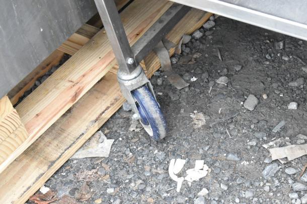Stainless steel table with drawer, under shelf, and commercial casters; shown is the sturdy caster wheel on rocky ground.