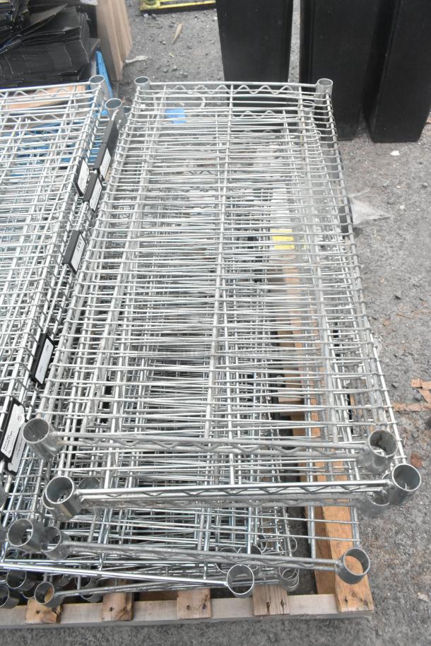 Lot of 30 chrome finish wire shelves, stacked on pallet. Sleek design, durable, ideal for versatile storage solutions.