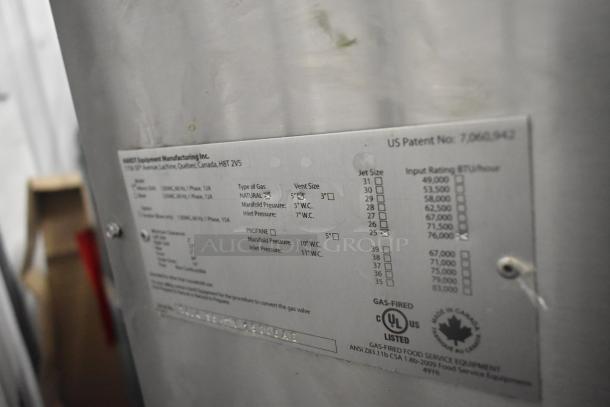 Hardt Inferno 3500 stainless steel commercial natural gas rotisserie oven with skewers, metal legs, and commercial casters. Visible label details gas type and vent size specifications.