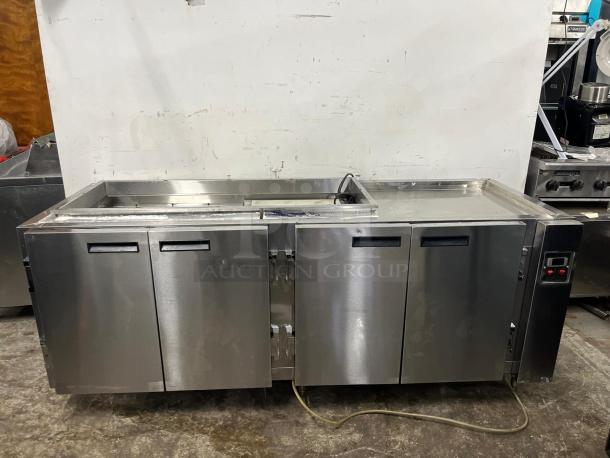Four-door stainless steel pizza prep table, features refrigerated storage and cutting surface. Good condition, plug visible.