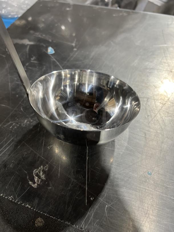 New Adcraft LD12 12 oz stainless steel ladle, commercial-grade, polished finish, in unused condition on metal surface.