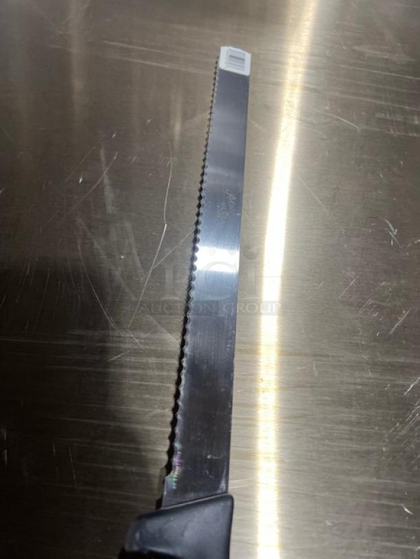 Commercial stainless steel serrated kitchen knife with black grip handle. Appears in good condition, bar code visible.