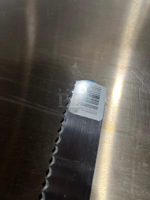 Commercial stainless steel serrated kitchen knife with black grip handle. Barcode label visible on the blade. Brand new condition.