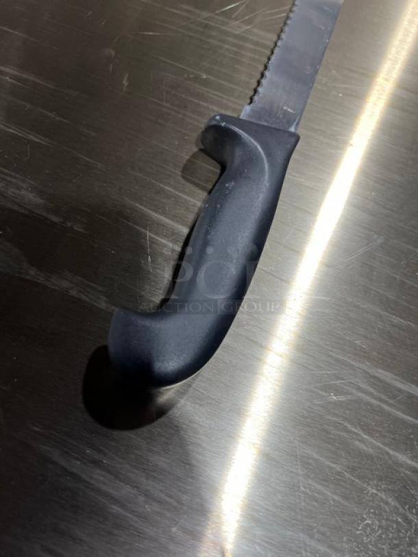 Commercial stainless steel serrated kitchen knife with black grip handle. Appears in excellent condition, ideal for heavy use.