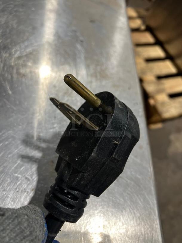 Close-up of plug for Merrychef eikone4s commercial convection oven, black casing, metal prongs, on stainless surface.