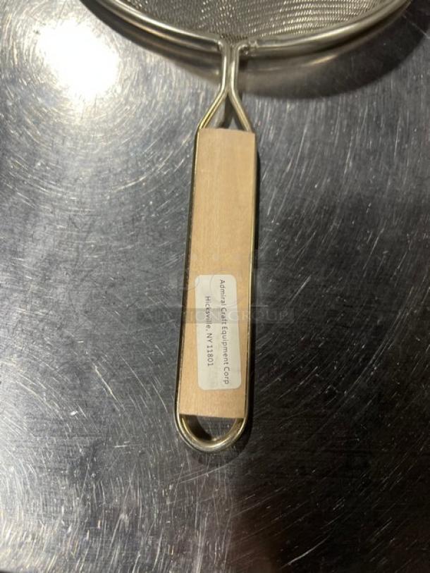 Adcraft commercial stainless steel strainer with wooden grip. New condition, durable design. Tag shows Adcraft address.